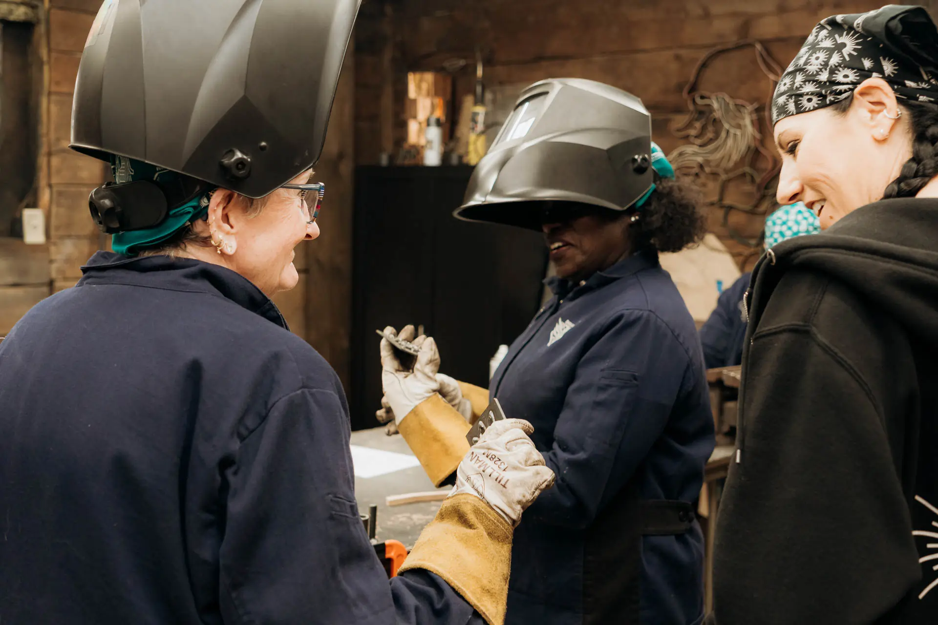 Participants in welding helmets laughing together while inspecting a piece