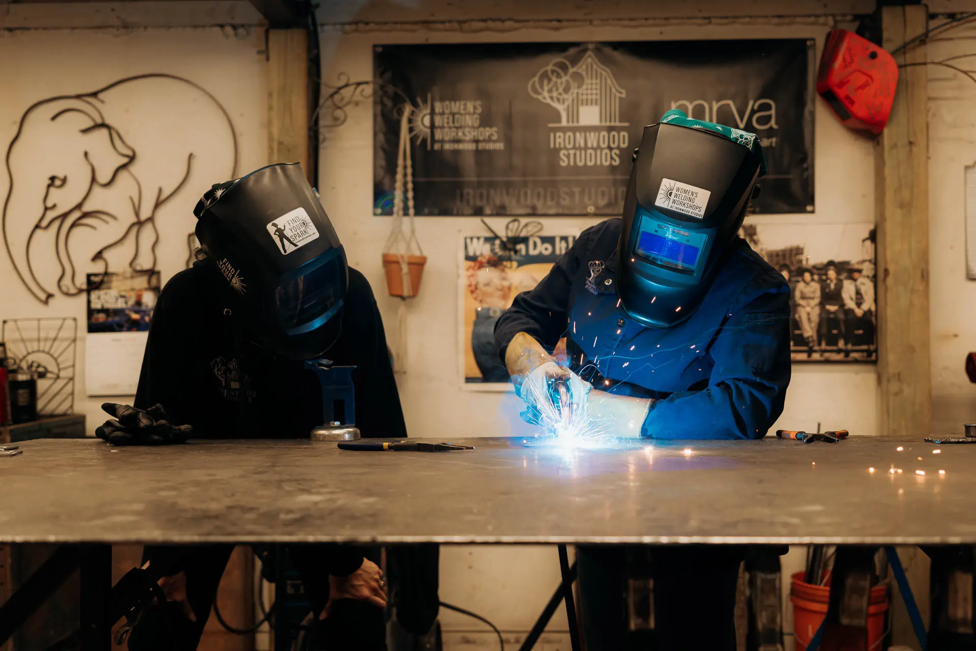Welder forging metal with bright blue sparks at Ironwood Studios